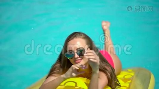 年轻女子20多岁，在暑假在游泳池附近放松。 比基尼女孩日光浴躺在充气床上视频