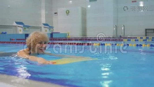 老年妇女带着特殊设备在游泳池游泳。视频