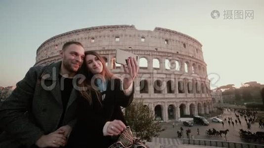 快乐的年轻夫妇在意大利罗马斗兽场附近自拍。 英俊的男人吻女人，微笑。视频