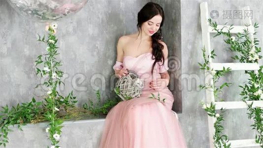 穿着粉红色长裙的迷人女士坐在植物工作室装饰的灰色角落里视频