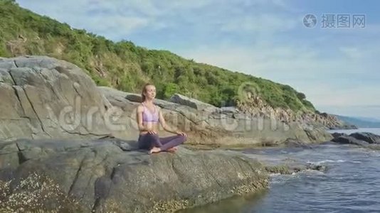 女孩专注于瑜伽姿势在岩石海滩对抗波浪视频