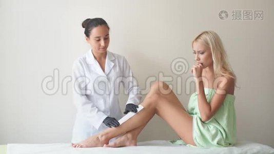 女性腿部和脱毛与热蜡疼痛程序。 在美容沙龙做脱毛的女人。 蜡脱毛视频