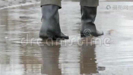 一个人穿着橡胶靴穿过泥泞的水坑。视频