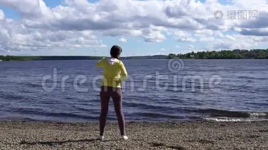 一位年轻妇女白天在湖岸从事健身活动。视频