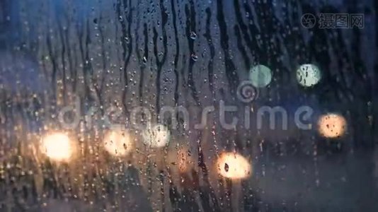 以模糊的夜晚城市汽车灯光为背景，在混合车窗玻璃上关闭雨滴。 4K.视频