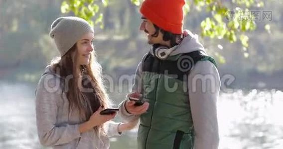 开朗的年轻情侣男人和爱说话的女人用手机户外日出，早秋公园视频