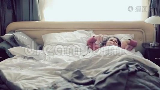 可爱的小女孩在床上醒来时微笑着快乐地伸展着手臂。视频