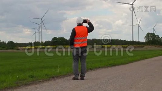 电动工程师在风车附近的智能手机上行走和拍照视频