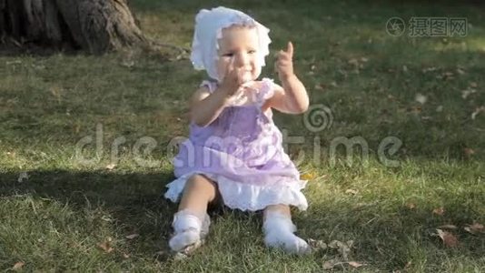 一个戴帽子的女婴坐在草地上拍手视频