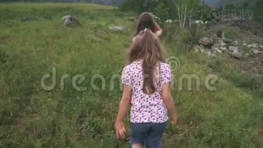 孩子们沿着草地走。 两个小女孩的旅行者走过一片靠近山河的田野视频