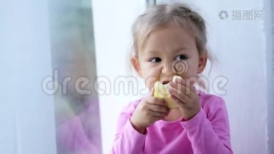 滑稽可爱的小女孩坐在窗台上吃苹果的肖像。视频