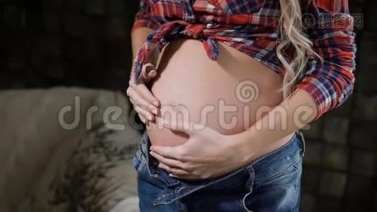 一个穿着蓝色牛仔裤和格子衬衫的快乐年轻孕妇迷人的腹部和手的特写。 美丽的未来视频