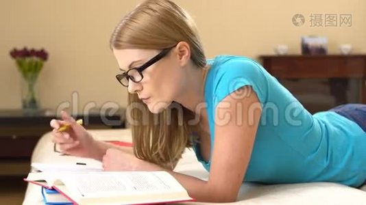 漂亮的大学生戴着眼镜躺在沙发上学习。 在笔记本上做笔记。视频
