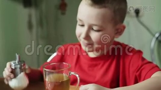穿红色衬衫的小男孩正通过勺子在茶杯中混合一颗糖。视频