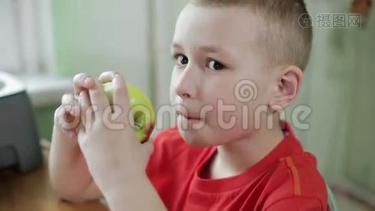 一个穿红色衬衫的男孩在厨房的桌子上吃苹果。视频
