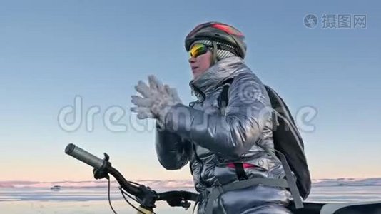 女人在冰上骑自行车。 女孩穿着银色羽绒服，自行车背包和头盔。 女人是视频