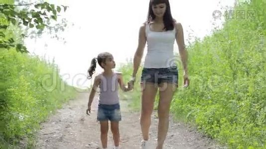 家庭价值观。 年轻的妈妈牵着小女孩的手在公园散步。视频