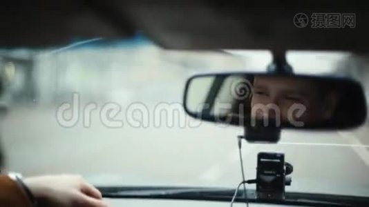 在城市里开车的时候对着镜子微笑的人。 英俊的男人的脸。 前窗上的雨滴。 开车旅行。视频