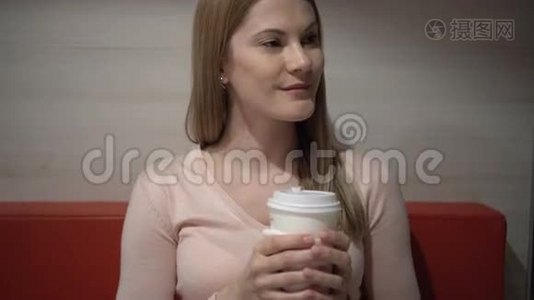 美丽迷人的年轻女人在咖啡馆里喝咖啡。 晚上好。 纸咖啡杯红色沙发视频