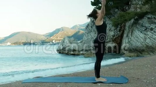 日落时分，一位年轻女子在海边的蓝色垫子上做瑜伽。视频