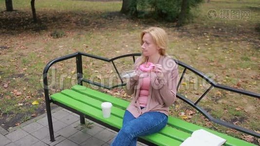 公园里的金发女孩吃甜甜圈。 户外女人吃甜面包视频