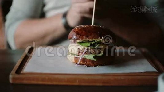 美味的汉堡在木制托盘上很棒。 一个人牵着手吃，尝一尝视频