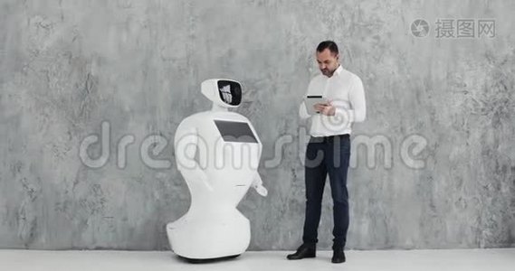 一个时尚的男人与机器人交流，把一只塑料机械手臂按在机器人身上，握手。 控制系统视频