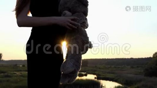 年轻的怀孕女孩在日落时和熊玩。视频