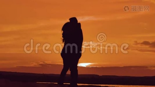 一对相爱的情侣在夕阳下拥抱剪影。 家庭爱情概念爱。 一对男女的爱情剪影视频