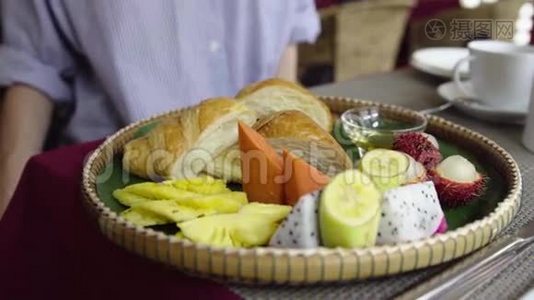 妇女早餐吃热带水果，牛角面包，薄饼和蜂蜜。视频