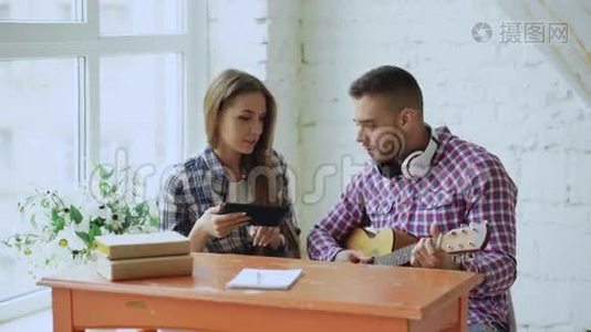 年轻、快乐、有爱心的一对夫妇学习用平板电脑弹声吉他，坐在那里玩得开心视频