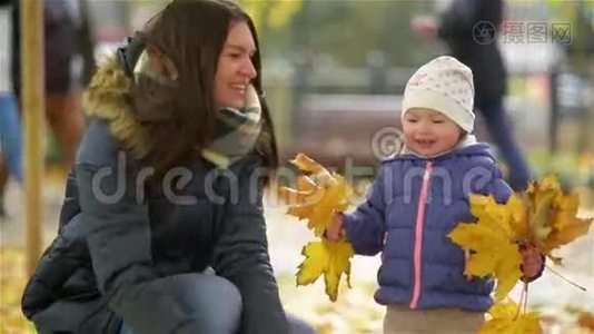 快乐的年轻妈妈和她的小女儿在秋天的公园里玩，妈妈和女孩扔树叶和笑视频