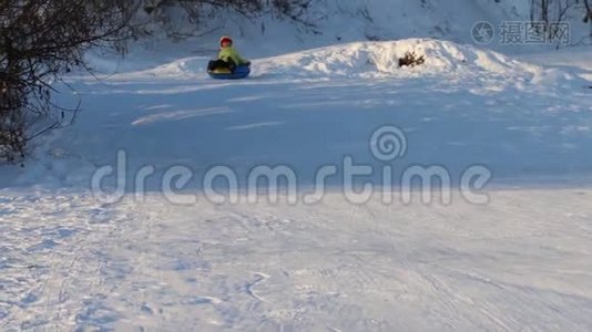 阳光明媚的冬日，快乐的女孩从雪筒滑下山坡视频