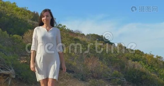 美丽的年轻女子在海边的荒山中散步。视频