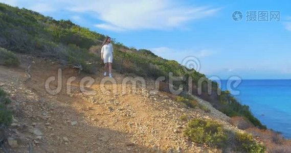 美丽的年轻女子在海边的荒山中散步。视频