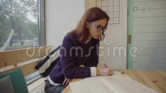 漂亮的女孩坐在桌子上，在笔记本上学习和写作视频