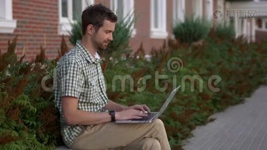 休闲着装的自由职业者坐在长凳上，用他的智能手表和笔记本电脑视频