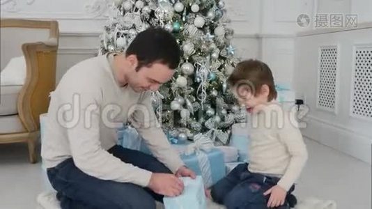 微笑的父亲和他快乐的儿子在圣诞树旁打开礼物视频