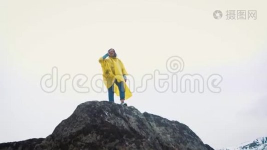 一个穿着黄色斗篷的年轻女孩沿着岩石跑。 一个旅行者正在山间旅行。视频