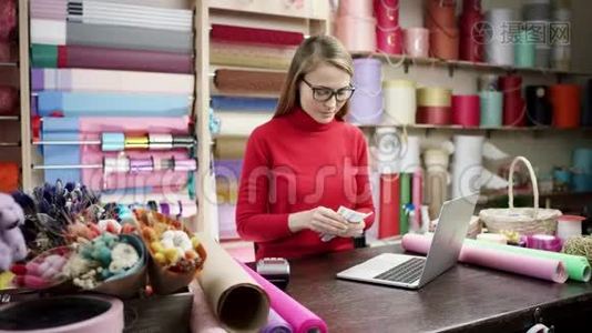 花店女花店女花匠在手机上聊天的同时使用笔记本电脑，在线查看订单.. 批发花卉销售视频