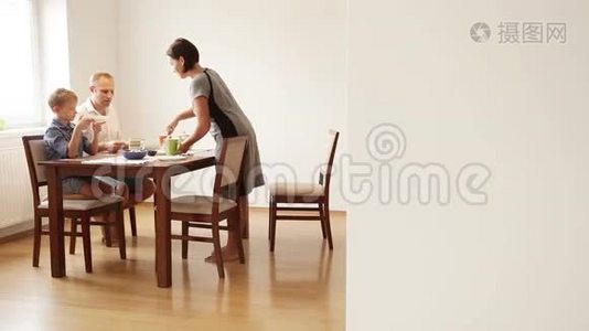 一家人在吃早餐：妈妈把煎蛋卷放在儿子和丈夫的盘子里视频