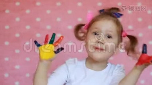 有趣的孩子用手掌在五颜六色的油漆。 快乐的小女孩画着肮脏的手。视频