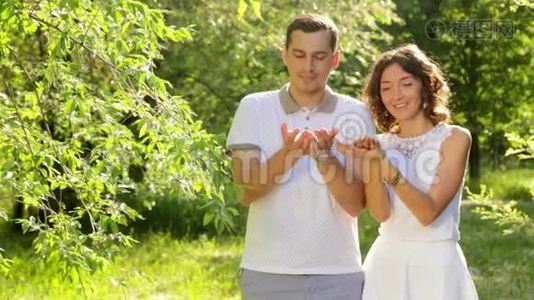 可爱的年轻夫妇吹蒲公英种子笑日落夏场视频