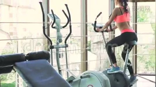 女孩在健身房里骑运动自行车做运动。 在她身后视频