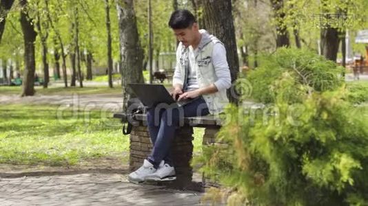 亚洲男人坐在公园里用笔记本电脑工作视频