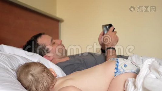 父亲在睡觉的婴儿附近的平板上读新闻。 一个男孩躺在床上房子的前景视频