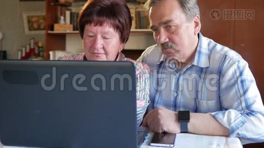 一对老夫妇坐在家里的笔记本电脑上。 一个女人看新闻，一个留着胡子的男人坐在他旁边说话视频