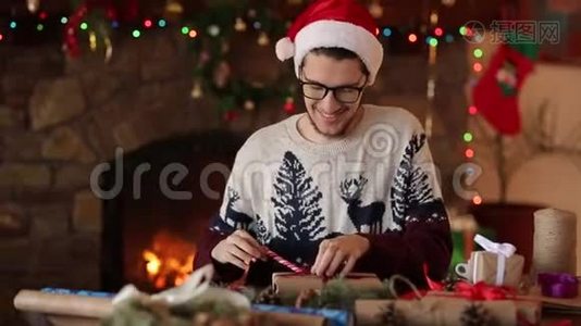 大胡子坐着，在壁炉旁的新年礼物上系上蝴蝶结。 戴着圣诞帽的家伙视频