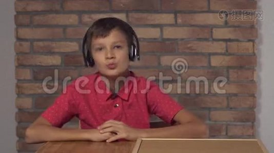 坐在书桌前的孩子拿着一张挂图，背景红砖墙上有刻字的音乐。视频