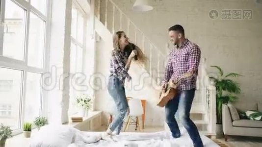 有趣的快乐和相爱的夫妇在床上跳舞，用电视控制器唱歌，弹吉他。 男人和女人在视频